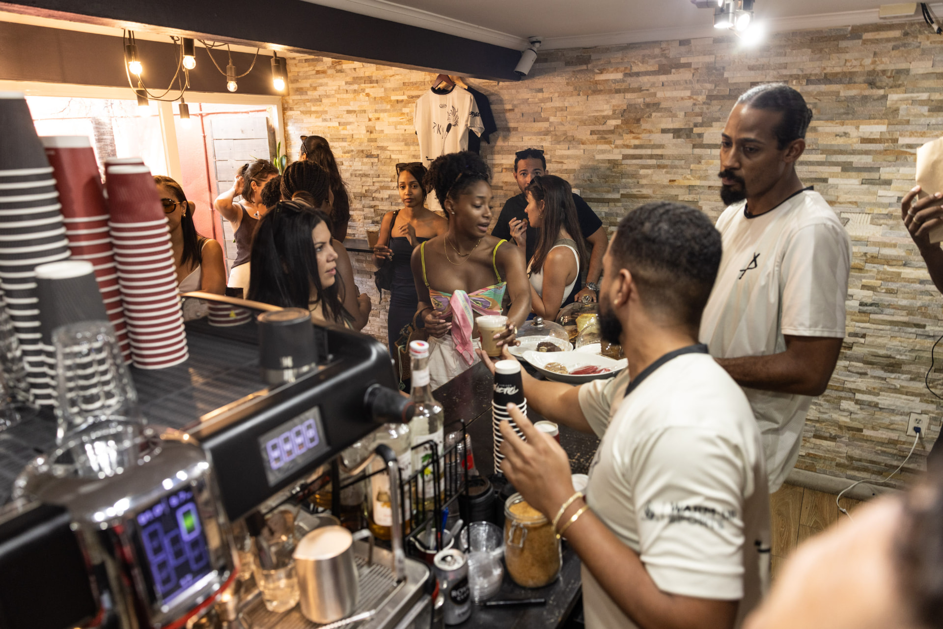 Busy night at the Pakaya Society bar — espresso machine, stacked cups, and neighbors gathered around the counter